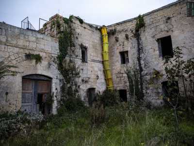 Raggiungiamo infine le spalle della masseria. L�edificio da questo lato sembra ancor pi� decadente rispetto alla facciata: i vari ingressi del piano terra sono ostruiti da erbacce e le crepe nelle pareti rendono tutta la struttura pericolante